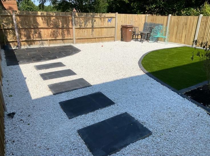 Black paving slabs set in white gravel with lawn and new fence